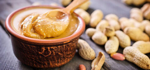 a bowl of peanut butter surrounded by unshelled peanuts.
