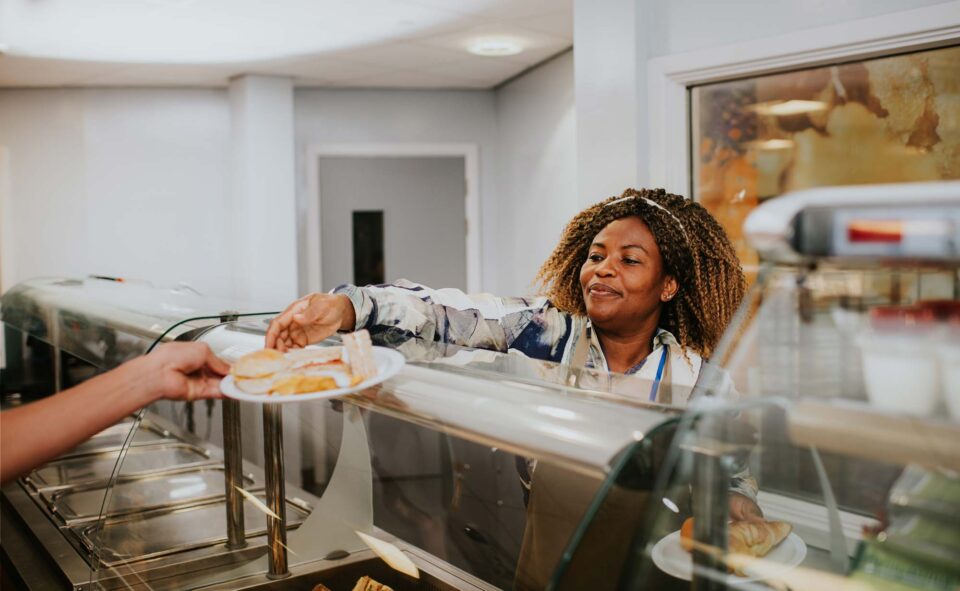 A friendly dinner lady serves college pupils food during lunch break in a cafeteria