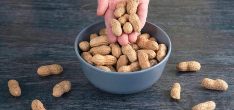 a person reaching for unshelled peanuts in a blue bowl.