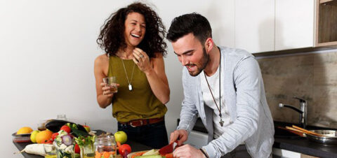 A man and woman having fun chopping vegetables.
