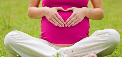 A pregnant woman making a heart shape over her belly with her hands.