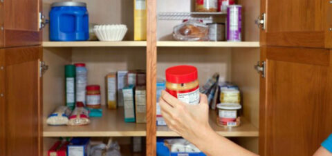 a woman holding a jar of peanut butter in a pantry.