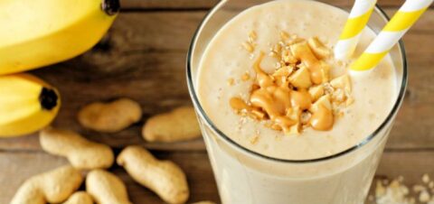 a cup filled with banana and peanuts smoothie with two straws popping out.