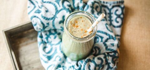 a tall cup of glass full of creamy smoothie with a straw popping out on top.