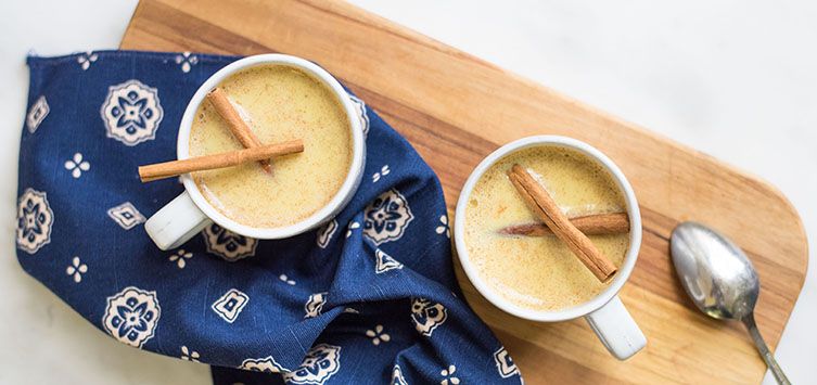 mugs filled with hot drink and decorated with two cinnamon sticks.