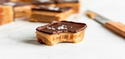a caramel bar topped with peanut butter and a thin layer of chocolate.