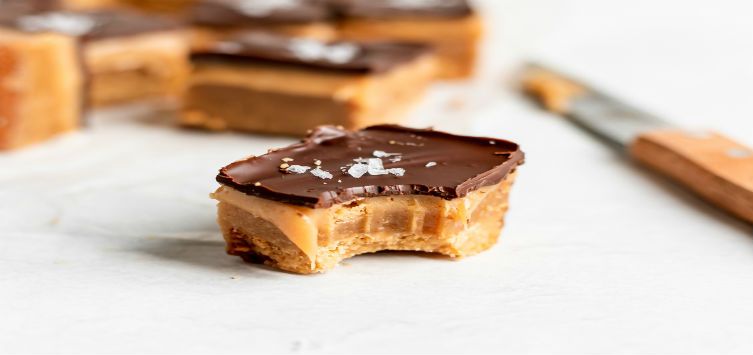 a caramel bar topped with peanut butter and a thin layer of chocolate.