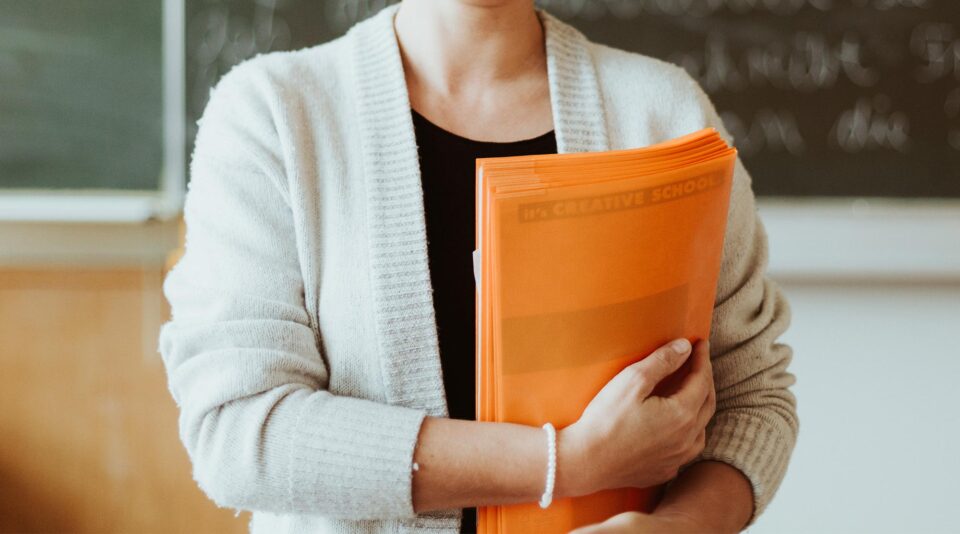 Female teacher in front of a chalkboard with exercise books in hands